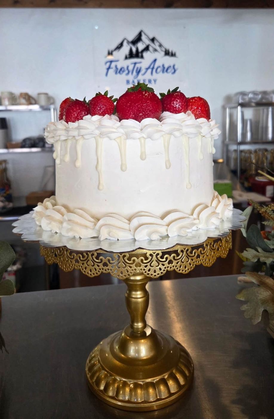 A white drip cake topped with fresh strawberries on a gold cake stand