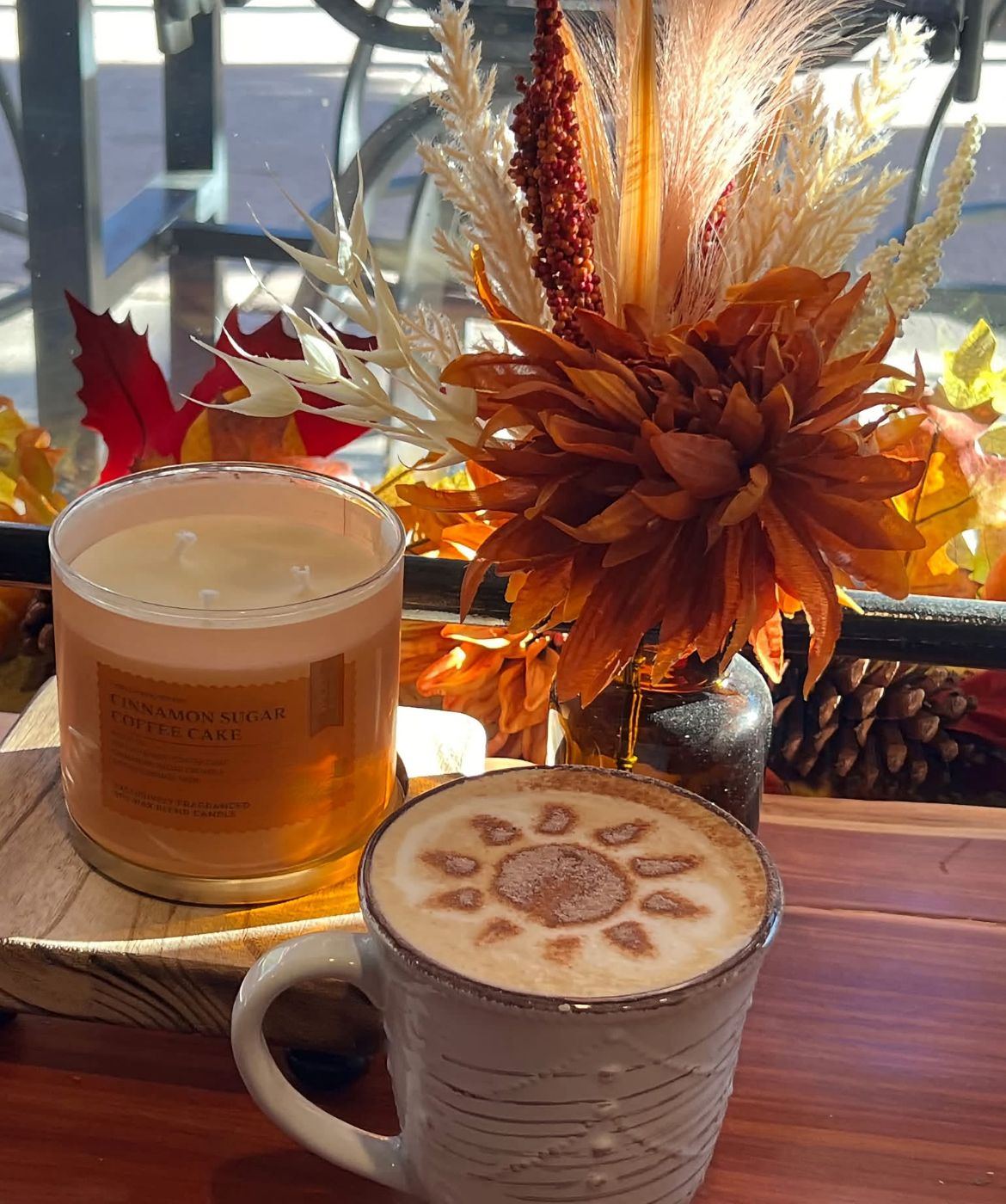 A latte with a sunflower pattern in the foam beside a fall candle