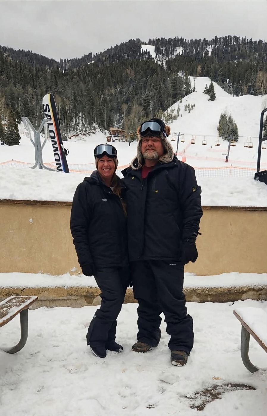 A couple in ski gear standing in the snow on the mountain